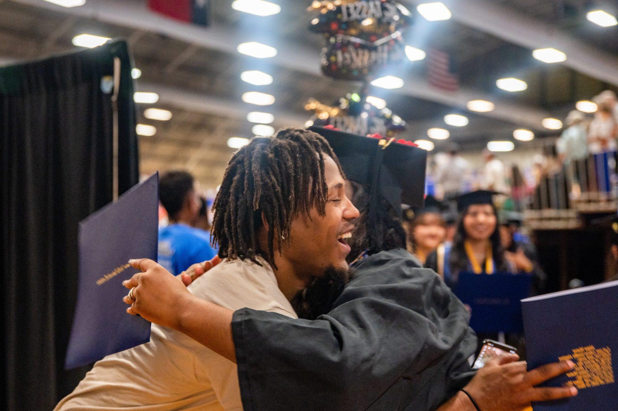 A student graduating and being hug by someone they know.